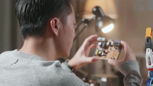 Over The Shoulder View Of A Male Holding And Looking At The Board While Repairing A Cyborg Hand