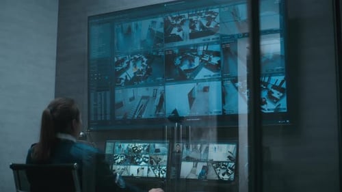 Una operadora de seguridad observa las cámaras de circuito cerrado de televisión con varios monitores y una gran pantalla digital