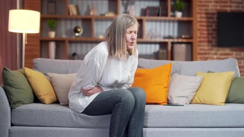 Woman Experiencing Abdominal Pain at Home on Sofa