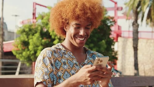 Close-up of young guy outdoors chating online, reading text on smartphone in his hands and smiling
