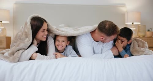 Happy Family Smiles from Under Blanket in Bedroom