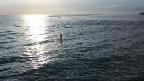 Paddleboarder and a surfer enjoying the calm waters around Reunion Island as the sun sets