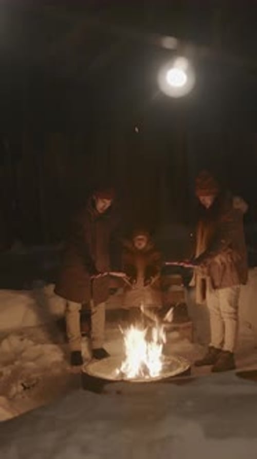 Parents and Kid Warming Hands on Campfire Outdoors on Winter Night