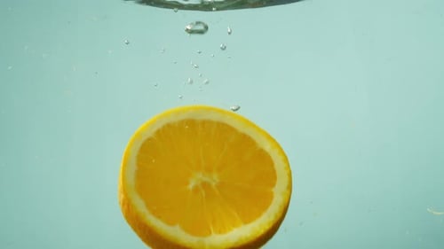 A Round Slice of an Orange Falls Into the Water on a Blue Background