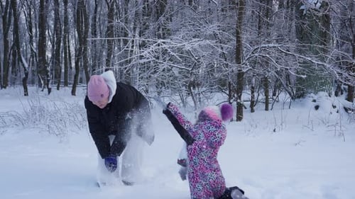 Woman and Child Playfully Throwing Snowballs in Snowy Forest
