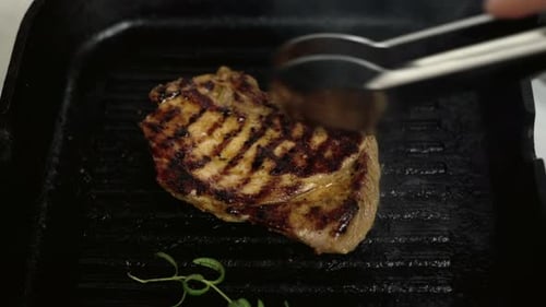 Cooking a beef stake with rosemary on a black pan at the kitchen at home, close up