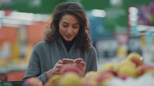 Woman Doing Grocery Shopping at the Supermarket and Using Phone Look at Camera Smile Internet