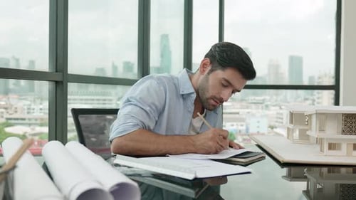 Architect Working on Plans in Office with Model