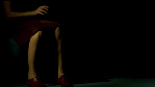 Woman Sits Still in a Chair in Dim Light