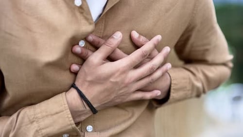 Close up. Male hands holding chest. Man in shirt has heart attack while sitting on bench on street