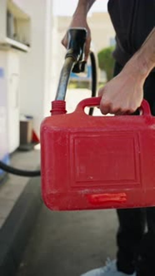 Man Filling a Red Plastic Canister with Fuel at a Gas Station