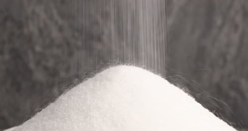 Pouring granulated sugar onto pile against grey background, closeup