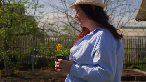 Woman Holds Potted Flower in Rural Garden