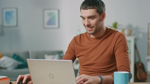 Smiling man uses laptop at desk in home