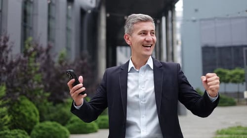 Excited Man Celebrating Success Using Smartphone Outside