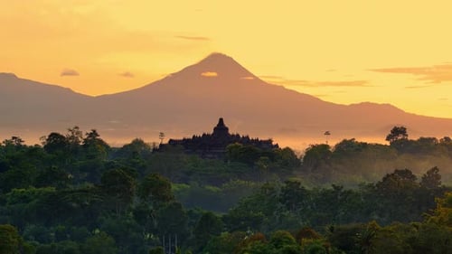 O maior templo budista de Borobudur ao pôr do sol com o monte Merapi atrás