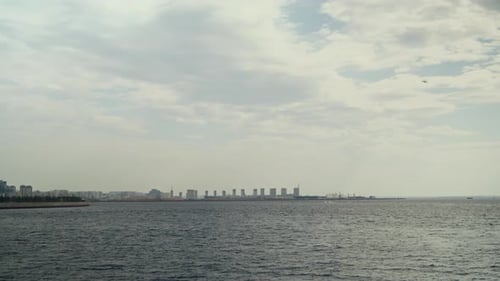 Wide Urban Seascape with City Skyline on Horizon under Cloudy Sky