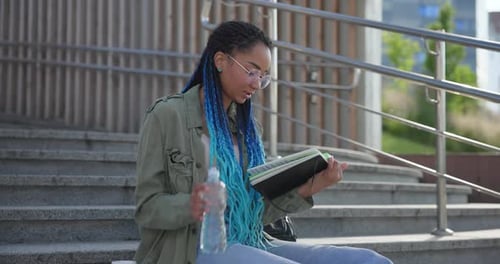 Woman Reading and Drinking Water on Urban Steps