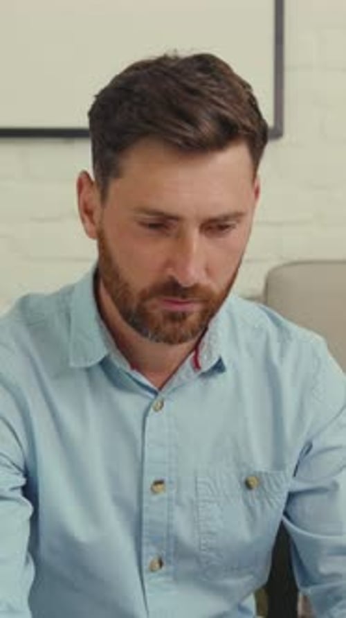 Ein bärtiger Mann in einem blauen Hemd arbeitet an einem Laptop und lächelt in die Kamera