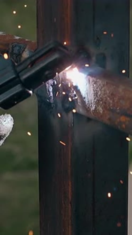 Closeup Worker Hand with Welding Machine Fixes Fence