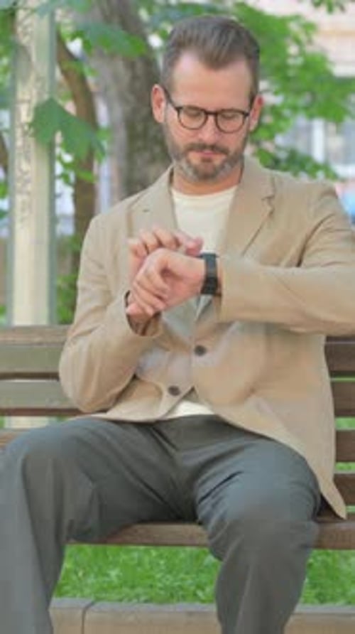 Man Sitting on Park Bench Checking Smart Watch