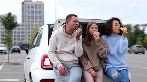 Family Eating Donuts at Car Trunk in City