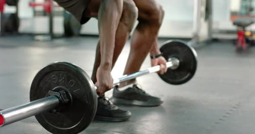 Bracing stance African American male trainee executing deadlifts while trainer guiding form at gym