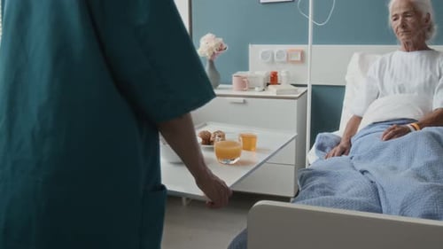 Nurse Pushing Table toward Senior Patients Bed Serving Meal for Her in Hospital