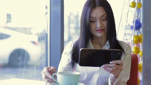 Woman Using Tablet and Drinking Coffee in Cafe