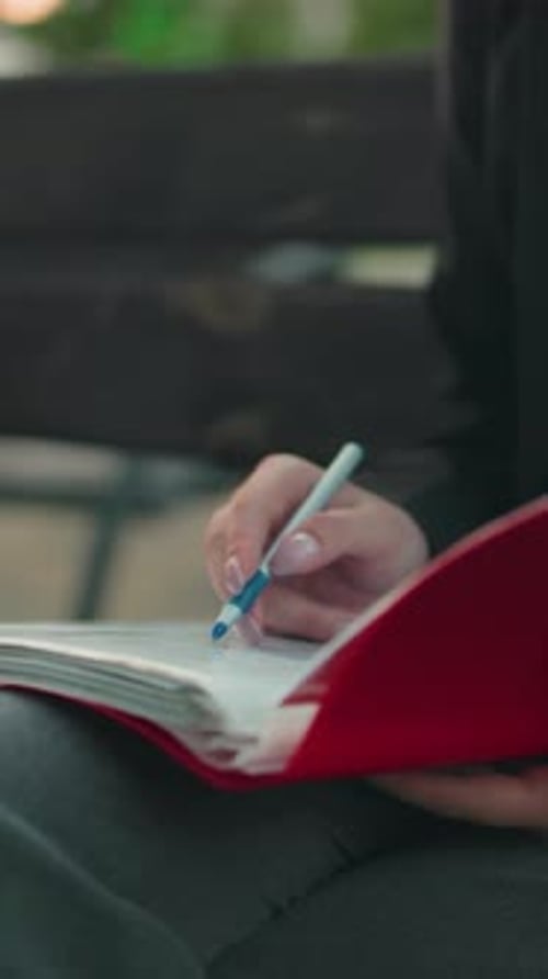 Professional Woman Reviewing Documents Outdoors with Pen and Laptop