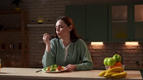 Woman Enjoying Healthy Salad in Warm Kitchen at Night