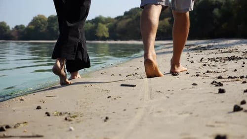 Bare Feet of Couple Stepping Together Along Sand Beach at Coastline Male and Female Legs of Pair