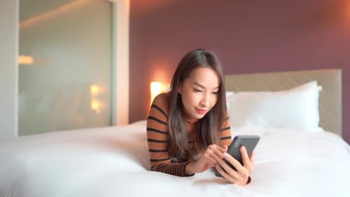 Young Woman Using Phone Lying on Bed