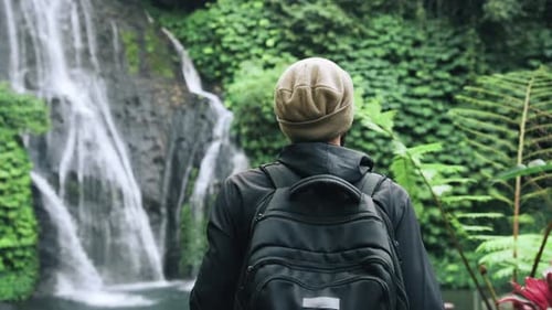 Traveling Man Walking in Green Nature of Forest Landscape to Mountain Waterfall