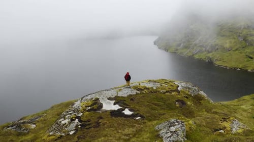 Attractive Girl in Trekking Clothes with Stands on Top of a Mountain Range and Looks Around High in