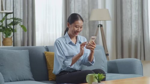 Young Woman Smiling and Using Smartphone at Home