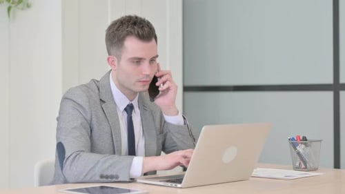 Young Adult Working in Office on Phone and Laptop