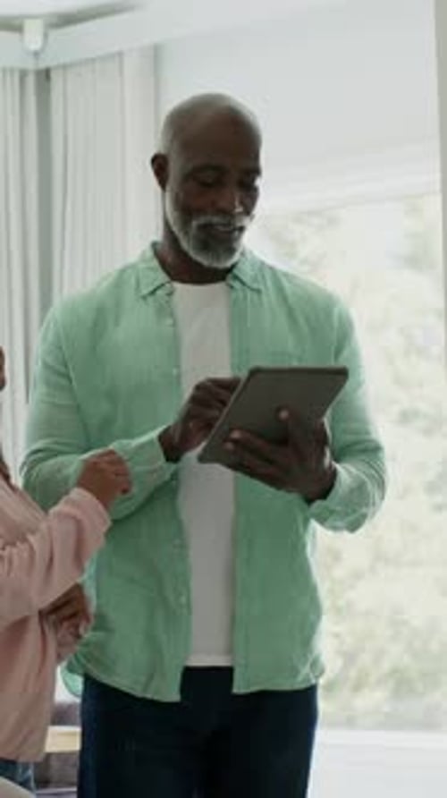 Vidéo verticale : tablette tapotant, homme mûr en chemise verte défilant par une fenêtre lumineuse, partageant sa joie