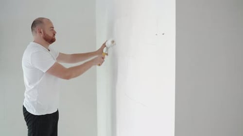 Man Paints White Wall with Roller in Room