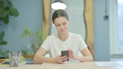 Young Woman Using Smartphone at Desk Indoors