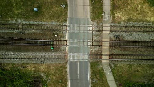 Vista aérea de um carro cruzando trilhos de trem em um cruzamento durante o dia, capturada em