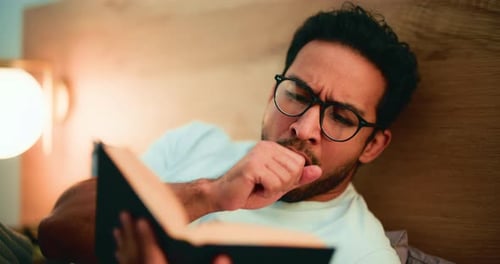 Young Man Reads Book in Bed at Night
