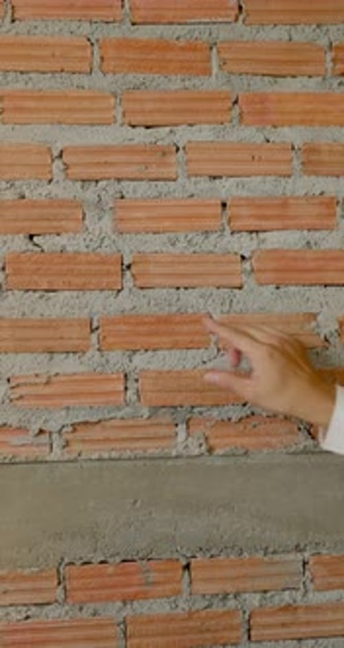 Close view of asian worker hand touching brick wall joint, checking masonry alignment, construction