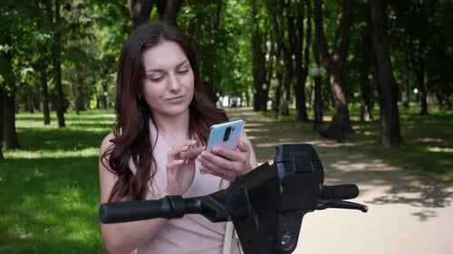 Woman Using Smartphone to Rent an Electric Scooter in City