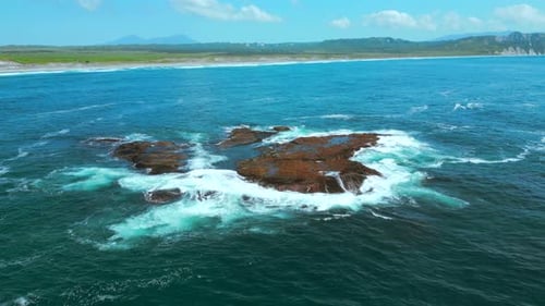 Aerial view of ocean waves crashing into rocks. Clip. Flying above turquoise water and giant boulder