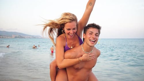 Joyful Couple Enjoying a Playful Piggyback Ride at the Beautiful Beach During a Sunny Summer Day