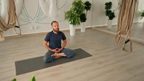 Adult bearded man in sportswear meditating doing breathing exercises during yoga class in the hall