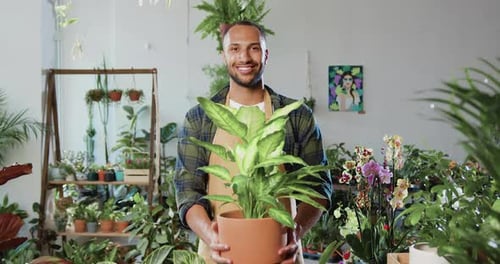 Portrait of good-looking contented botanical gardener worker in uniform standing in flower store