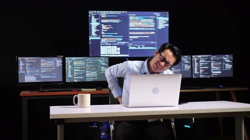 Asian Male Programmer Having A Backache While Writing Code By A Laptop Using Multiple Monitors
