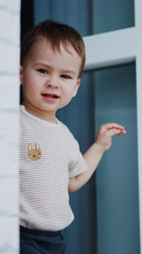 Un adorable petit garçon apparaît sur le balcon en faisant des grimaces sous une lumière vive.